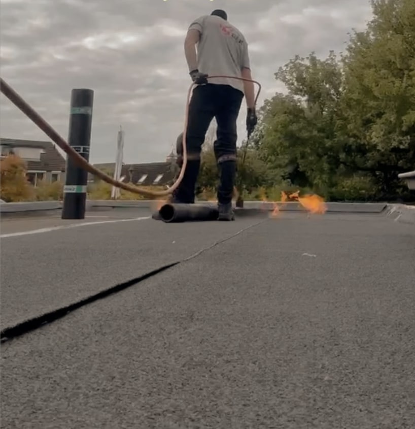 Dakdekker van TakDak brandt een baan bitumen op een plat dak