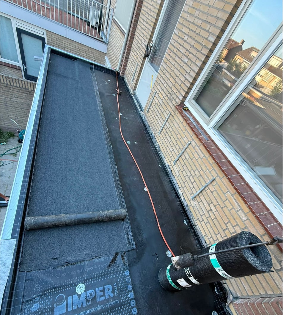Plat dak tijdens de renovatie: de onderlaag ligt er, de eerste baan van de toplaag wordt gebrand